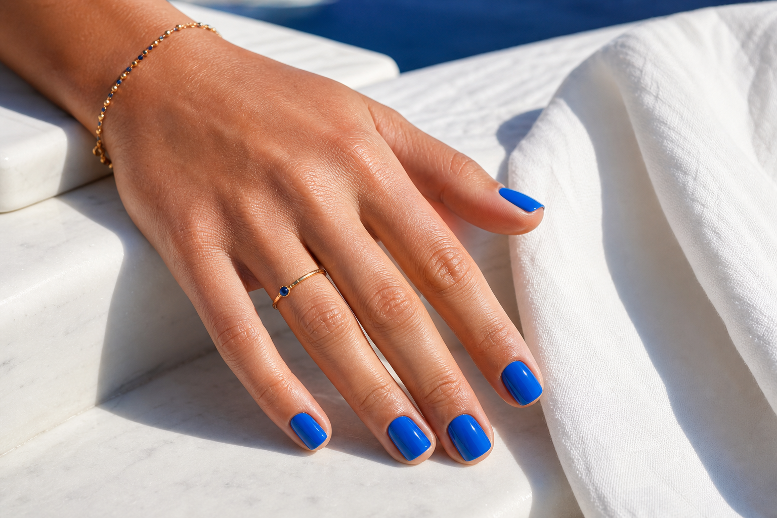 Azure manicure beside white Greek marble and gold jewellery