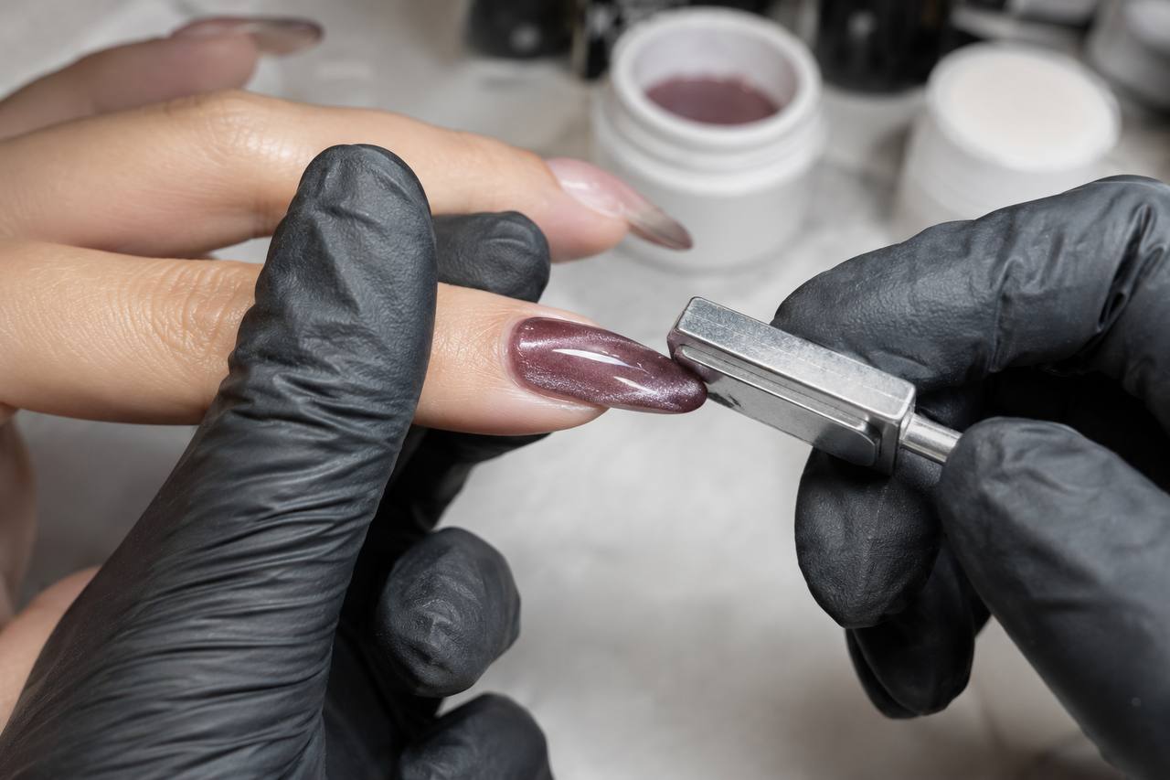 Technician positioning magnetic gel particles on a burgundy cat-eye manicure